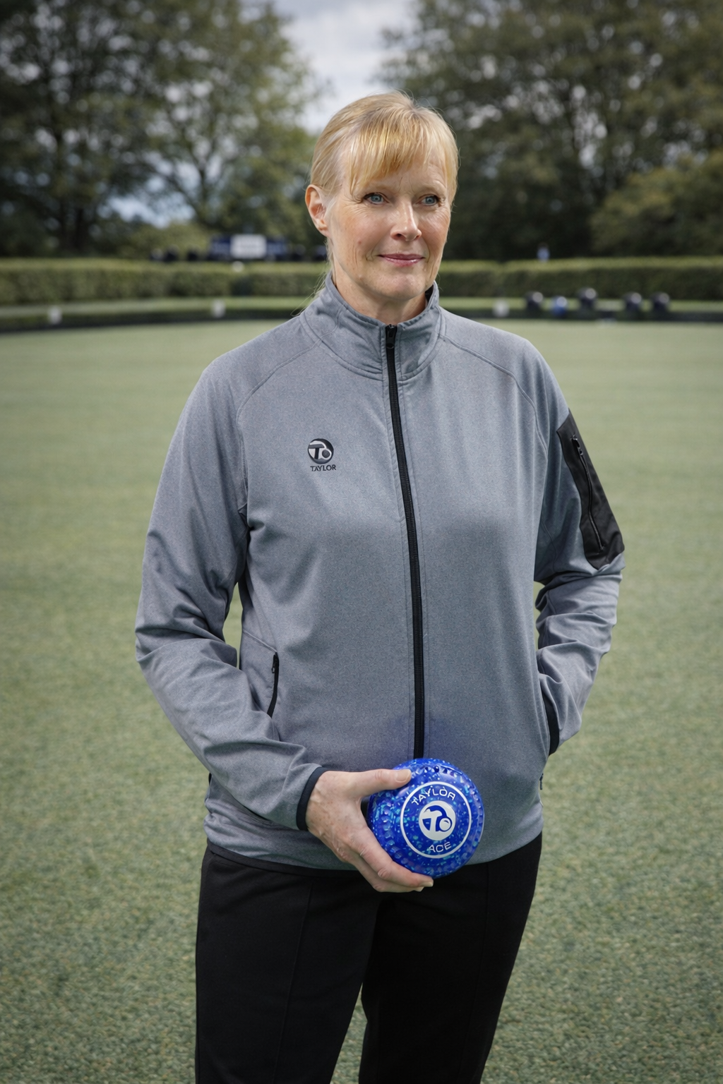 Woman in a gray jacket holding a blue object on a grassy field